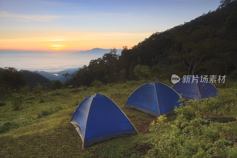 在泰国清迈的Doi Ang Khang日出时，在以山为背景的小山上露营帐篷